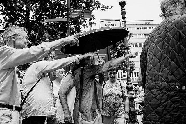 Das Bild zeigt mehrere, ältere Touristen auf der Place d’Armes mit ihrem Stadtführer, die alle in eine Richtung zeigen